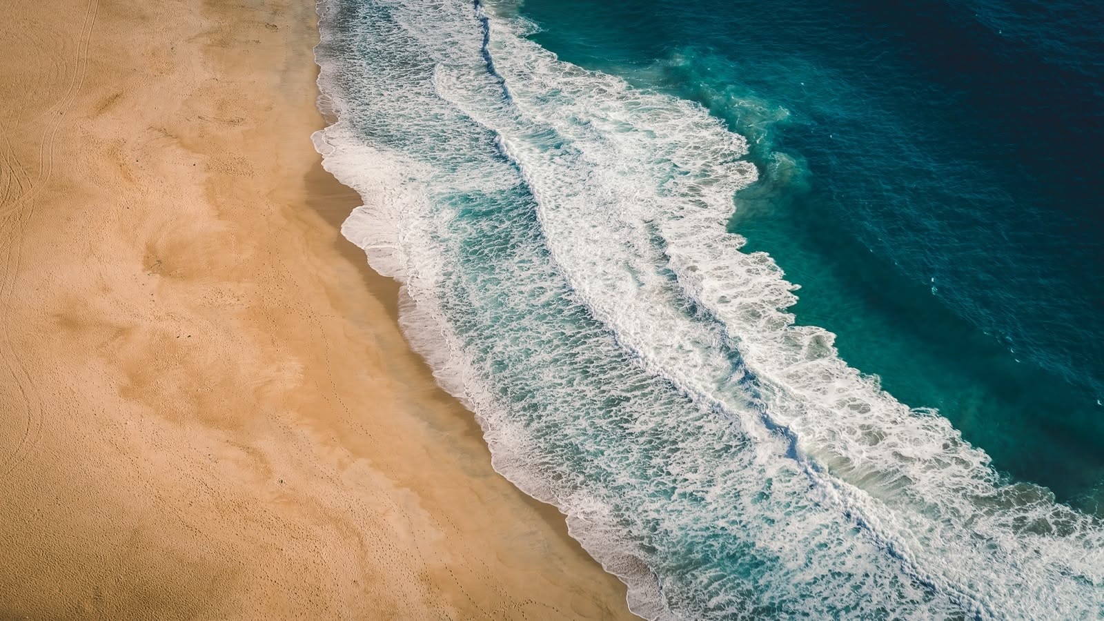 Aerial view of golden sand and turquoise ocean waves with white foam along the shoreline